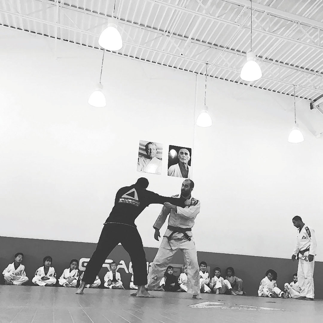 Two gym members spar on gym floor in front of young audience